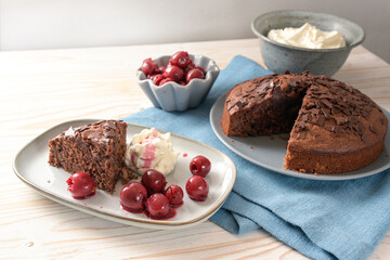 Homemade chocolate cake with morello cherries and whipped cream on a blue napkin and a bright wooden table, copy space, selected soft focus