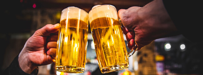 Close-up view of a two glass of beer in hand. Beer glasses clinking in bar or pub