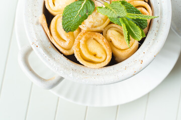 Beautiful serving of stuffed pancakes in a white ceramic pan with raspberry jam and sour cream garnished with mint on a white background. Nice breakfast and dessert. View from above.