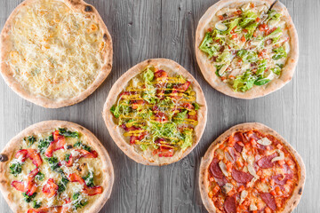 Assortment of pizza with meat, salami, prosciutto, tomatoes, dorblu cheese, mozzarella, parmesan, salad, spinach, red fish on wooden boards. Four cheese pizza, caesar, top view.