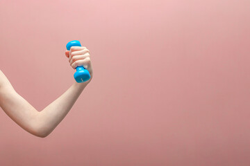 Fototapeta na wymiar Boy's hand holding a dumbbell on a pink background.Sports concept. Banner ,postcard and panoramic edition. copy space text