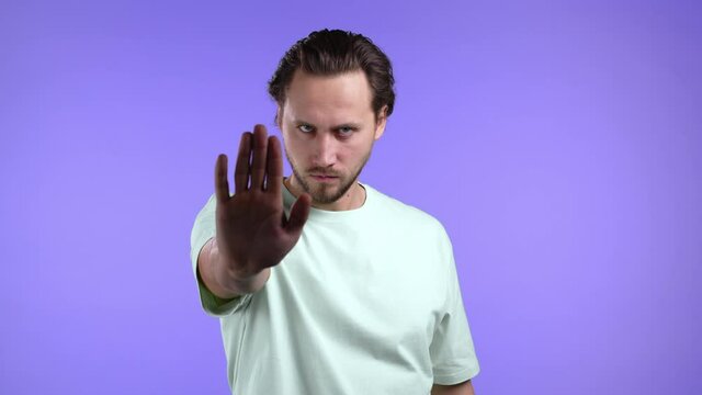 Portrait of serious man disapproving with no hand sign make basta, negation, enough gesture. Denying, Rejecting, Disagree. Portrait of handsome guy on violet background