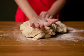 Little girl kneads dough with her hands on table at home. Child prepares dough for pizza, pie, dumplings, cookies in kitchen.