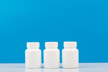 Three white medication bottles on white table against blue background with copy space. Concept of vitamins, supplements, medication and healthcare. 