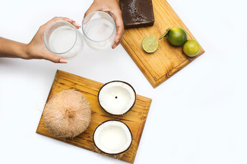 Fototapeta na wymiar Woman's hands hold panela of sugar cane, lemons and coconuts on a wooden board on a white background. lemongrass and coconut water are tropical drinks from the Caribbean