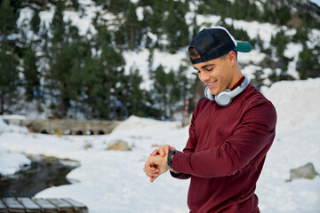 Smiling male athlete checking time in smartwatch while standing on snowfield