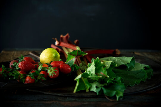 Studio shot of fresh rhubarb stalks, strawberries and single lemon