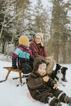 Family with Border Collie sitting on sled at snow covered field during weekend