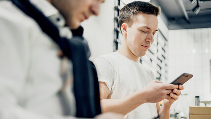 Men drink coffee and communicate in the messenger on the phone. A distance of 1.5 meters between two customers of a friend and people in a restaurant. Spend time in a cafe