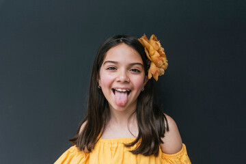Close-up of girl wearing yellow headband sticking out tongue against black background