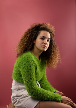 Fashionable woman with blank expression sitting by coral colored background