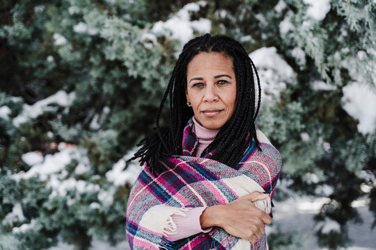 Mature woman with arms crossed wrapped in plaid shawl at park