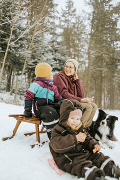 Smiling mother with daughter sitting while spending weekend with family and Border Collie during winter in snow