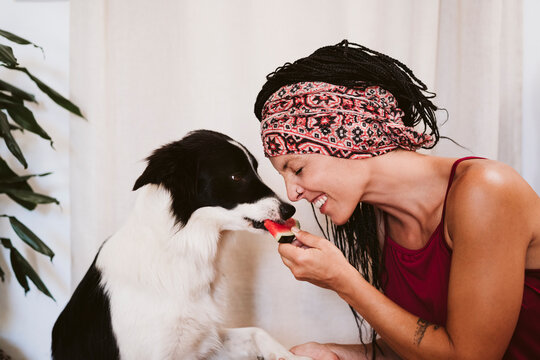 Woman smiling while feeding fruit to dog while sitting at home