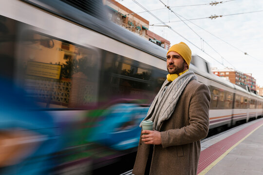 Mid adult man wearing knit hat holding coffee cup while standing at station