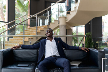 Male professional laughing while sitting on sofa in hotel lobby