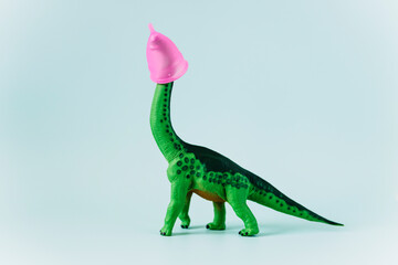 Diplodocus dinosaur toy with pink menstrual cup on the head on mint green background
