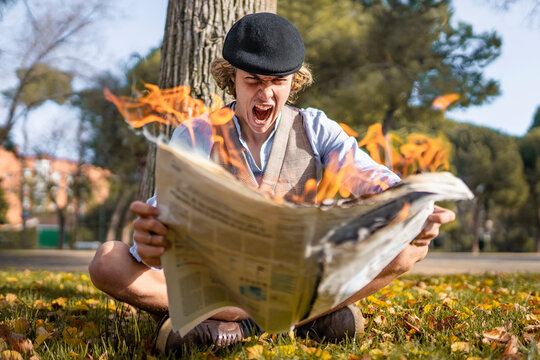 Screaming young man looking at lit newspaper while sitting in park