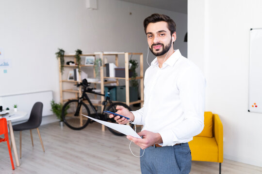 Smiling male professional with paper document holding mobile phone while working at work place
