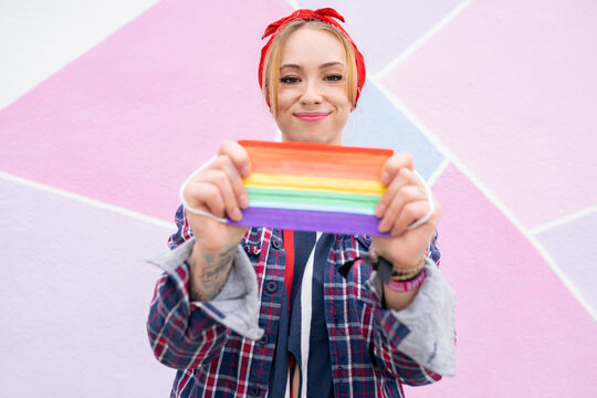 Smiling woman wearing headband holding multi colored face mask while standing against wall