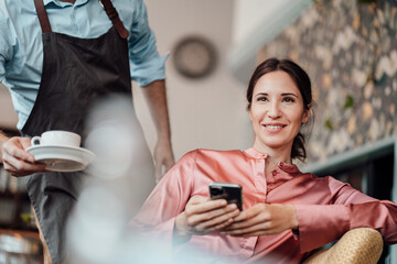 Male waiter serving coffee cup to smiling businesswoman at cafe