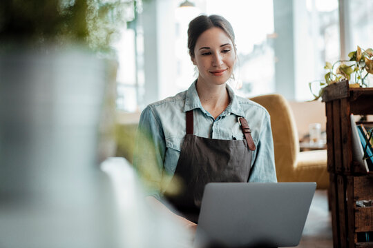 Smiling cafe owner working on laptop at table