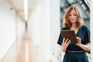 Senior businesswoman using digital tablet while standing in corridor