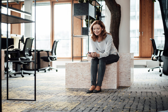 Female entrepreneur using smart phone while sitting on retaining wall at office