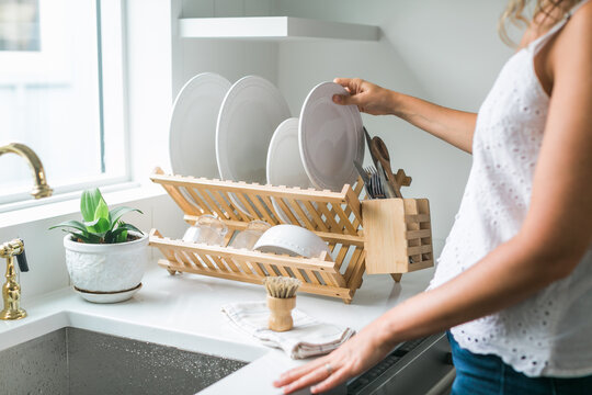 Woman washing dishes in kitchen using eco friendly brush and drying rack
