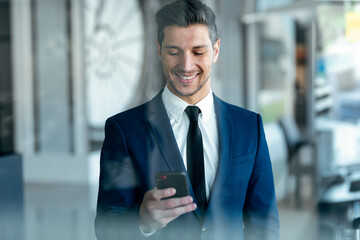 Smiling entrepreneur wearing suit using mobile phone while standing in office