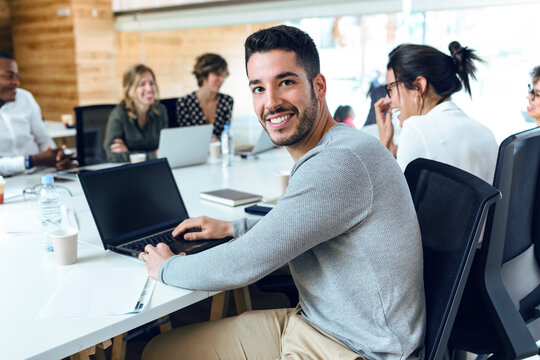Smiling businessman sitting by colleagues at conference table in board room during meeting