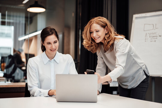 Happy businesswoman discussing with female colleague at conference table during meeting in office