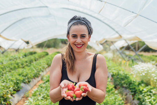 Happy beautiful female farmer holding fresh strawberries at organic farm