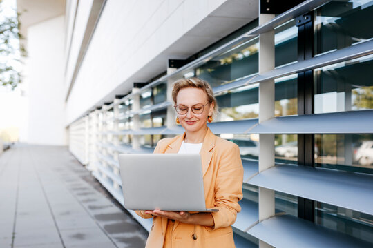 Female entrepreneur using laptop while standing against office building