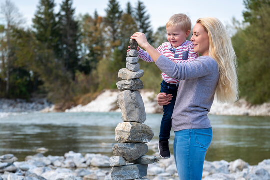 Mother carrying son while balancing stack of stones at riverside