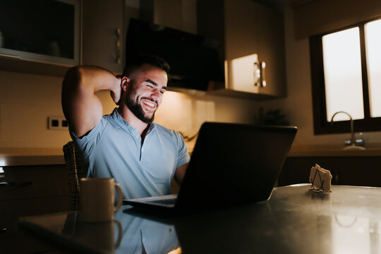 Smiling businessman with hands behind head while working on laptop at dining table at home