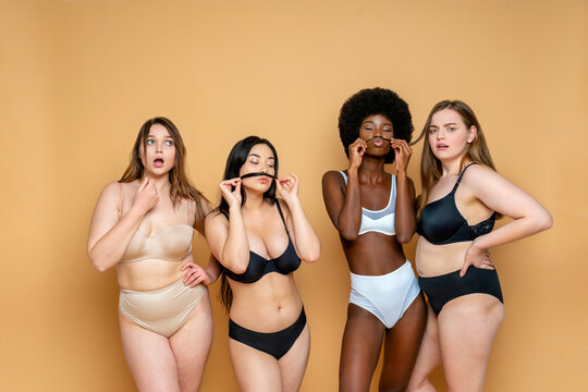 Multi-ethnic group of female models in lingerie standing against yellow background
