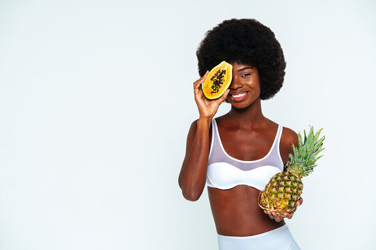 Afro young woman wearing lingerie holding papaya and pineapple against white background