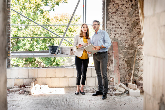Businesswoman with digital tablet looking away while working with engineer at construction site