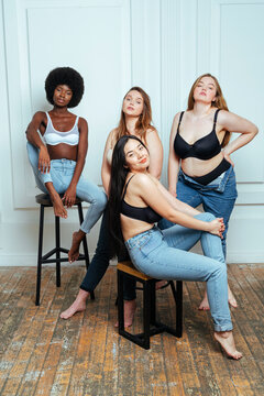 Confident multi-ethnic group of women in bras and jeans posing against wall