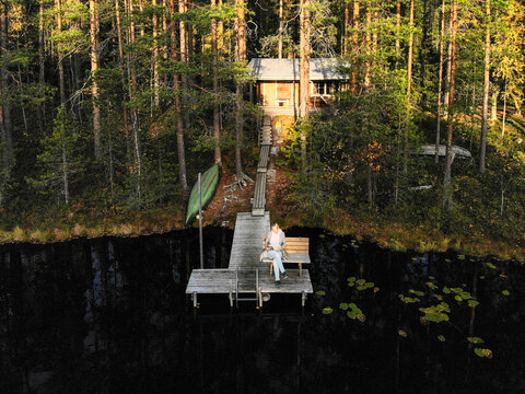 Drone shot of woman reading book while sitting on pier over lake in forest