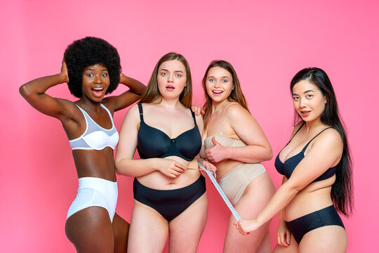 Surprised group of multi-ethnic female model in lingerie with tape measure against pink background