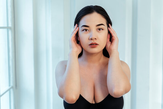 Plus size model with hand in hair wearing black bra against white wall