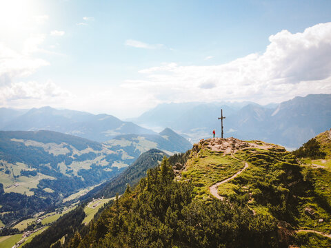 Drone shot of woman standing on mountain peak against sky during sunny day