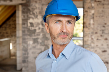 Confident architect wearing hardhat staring while standing at construction site