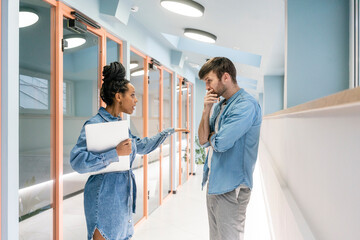 Young businesswoman with laptop arguing with male colleague in corridor at workplace