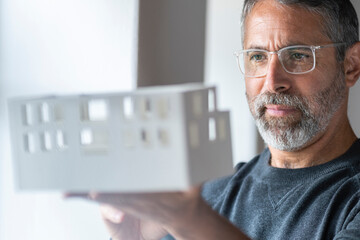 Businessman wearing eyeglasses examining architectural model while standing at home