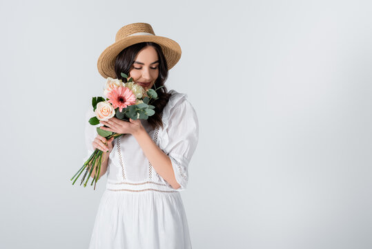 young woman in straw hat and dress holding bouquet of spring flowers isolated on white