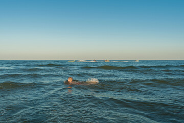The boy floats to the left, two jet skis are sailing to the right. Beautiful blue sea and sky after sunset