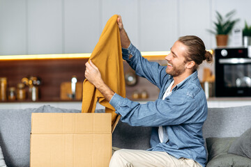 Smiling attractive man unpacked his parcel, happy about getting a long expected order. Caucasian...